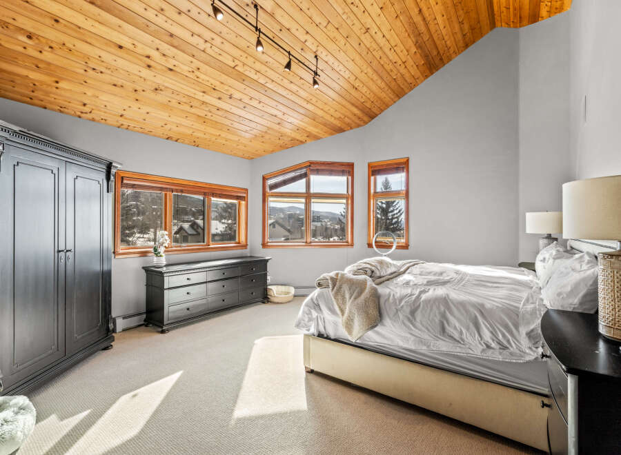 This stunning bedroom boasts a warm, inviting ambiance with its wooden ceiling and ample natural light.