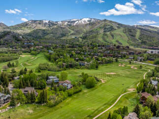 Experience luxury mountain living with this stunning aerial view of a golf course community nestled against a majestic mountain backdrop.