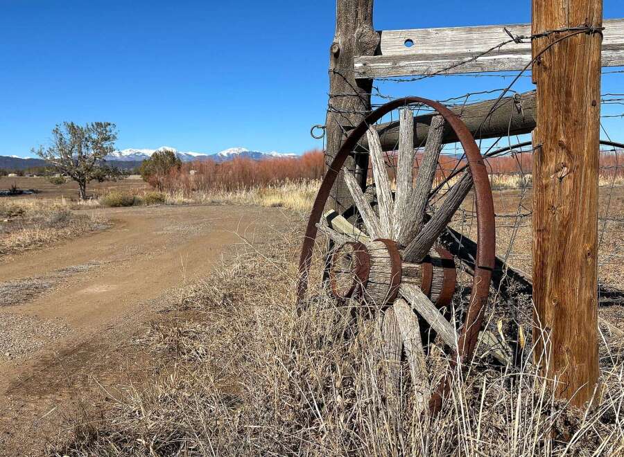 Discover the charm of this rustic property, featuring a weathered wagon wheel and a classic wooden fence.