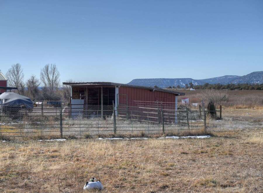 Discover the charm of this rural property, featuring a rustic red shed and expansive views of the surrounding landscape.