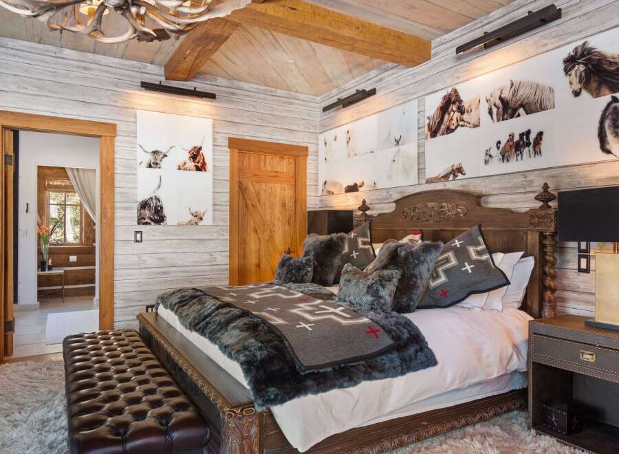 This luxurious bedroom showcases rustic elegance with its wood-paneled walls and ceiling, complemented by a stunning antler chandelier.