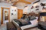 This luxurious bedroom showcases rustic elegance with its wood-paneled walls and ceiling, complemented by a stunning antler chandelier.