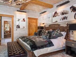 This luxurious bedroom showcases rustic elegance with its wood-paneled walls and ceiling, complemented by a stunning antler chandelier.