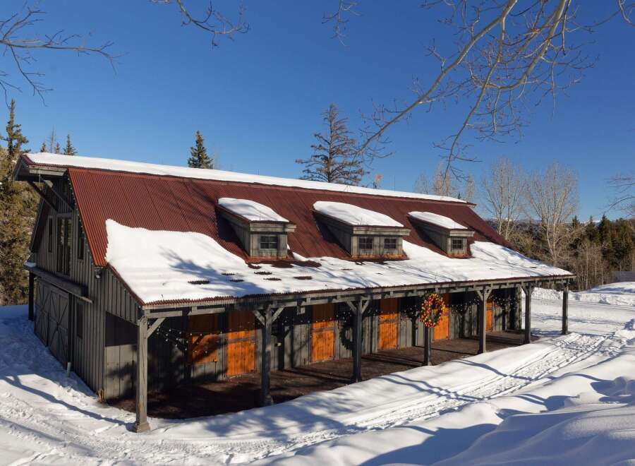 Nestled in a winter wonderland, this charming property boasts a rustic barn-style structure with a striking red corrugated metal roof.