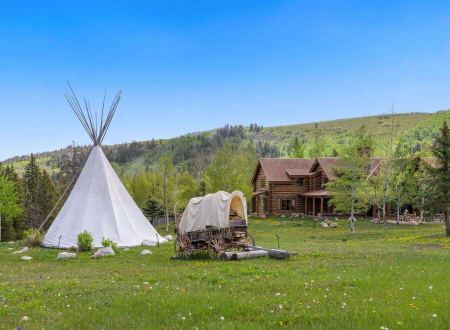 Escape to your dream retreat! This stunning property features a charming log cabin, a traditional teepee, and a covered wagon, all set against a backdrop of rolling hills and lush greenery.