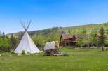 Escape to your dream retreat! This stunning property features a charming log cabin, a traditional teepee, and a covered wagon, all set against a backdrop of rolling hills and lush greenery.