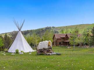 Escape to your dream retreat! This stunning property features a charming log cabin, a traditional teepee, and a covered wagon, all set against a backdrop of rolling hills and lush greenery.