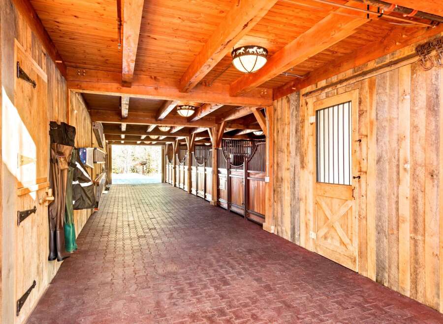 Experience the rustic charm of this beautifully crafted wooden barn, featuring a long, covered walkway with brick pavers and multiple horse stalls.