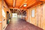Experience the rustic charm of this beautifully crafted wooden barn, featuring a long, covered walkway with brick pavers and multiple horse stalls.