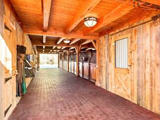 Experience the rustic charm of this beautifully crafted wooden barn, featuring a long, covered walkway with brick pavers and multiple horse stalls.