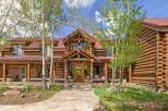 Experience rustic luxury in this stunning log cabin home, featuring a grand entrance with a natural stone pathway and a charming teal front door.