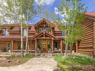 Experience rustic luxury in this stunning log cabin home, featuring a grand entrance with a natural stone pathway and a charming teal front door.