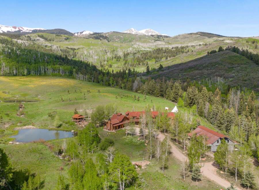Discover this stunning mountain retreat featuring a sprawling log home with a rustic charm and a picturesque pond.