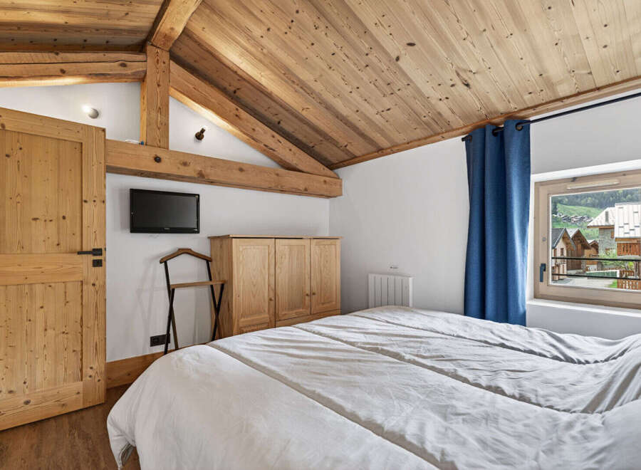 This charming bedroom features a cozy, rustic design with wooden beams and a sloped ceiling.