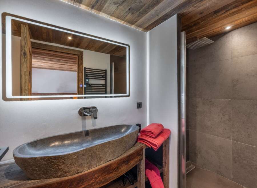 Experience luxury in this stunning bathroom featuring a unique stone sink and a modern, illuminated mirror.