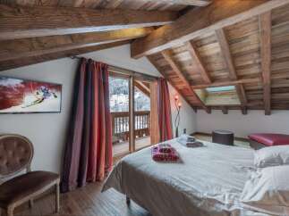 Experience the charm of this cozy bedroom featuring a rustic wooden ceiling and a private balcony with stunning mountain views.