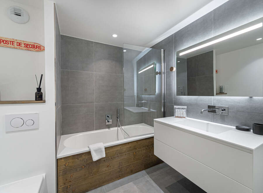 This modern bathroom features a sleek design with gray tiled walls and a white vanity.