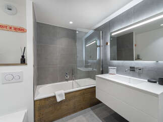This modern bathroom features a sleek design with gray tiled walls and a white vanity.