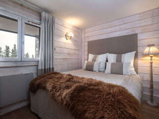 Experience cozy mountain living in this charming bedroom featuring rustic wood-paneled walls and a plush, warm throw blanket on the bed.