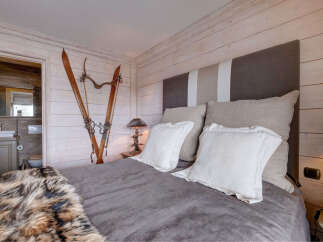 Experience rustic charm in this cozy bedroom, featuring vintage skis mounted on a whitewashed wood-paneled wall.