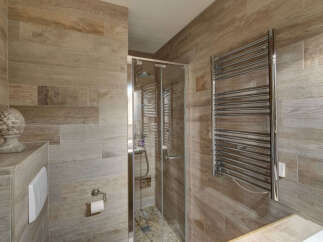 Experience modern luxury in this beautifully appointed bathroom, featuring a sleek glass-enclosed shower with a rainfall showerhead and a stylish chrome towel warmer.