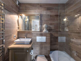 This modern bathroom features a sleek vanity with a vessel sink, complemented by wood-look tile walls and a chrome heated towel rack.