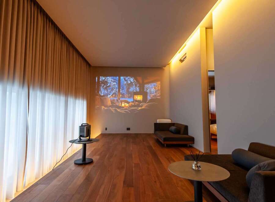 Experience luxury living in this stunning property featuring a cozy living room with a projector screen displaying a winter scene.