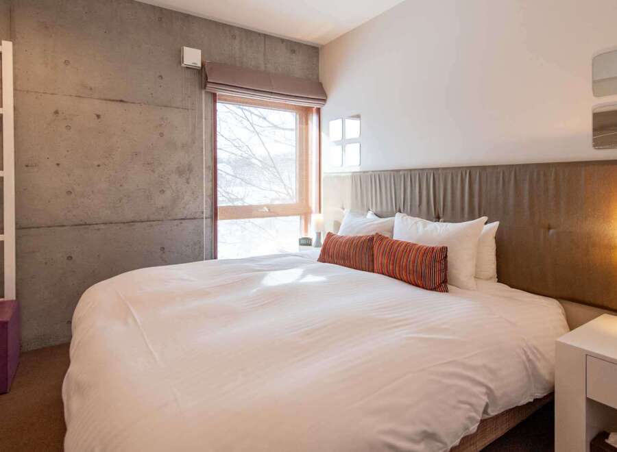This modern bedroom boasts a sleek design with a concrete accent wall and a large window that floods the space with natural light.