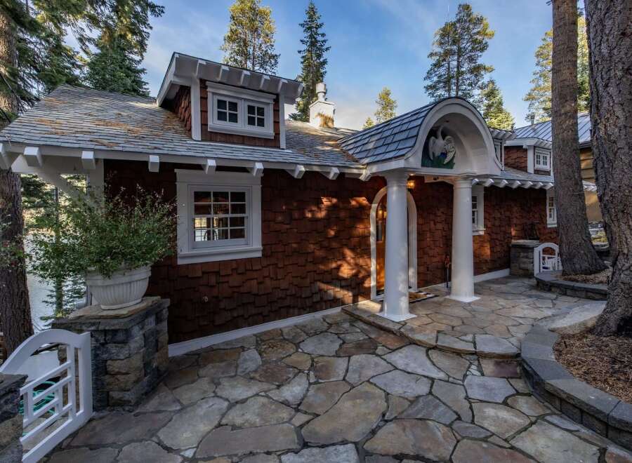 Nestled amidst towering trees, this charming property boasts a unique architectural design with a shingle exterior and inviting stone pathway.