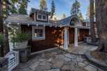 Nestled amidst towering trees, this charming property boasts a unique architectural design with a shingle exterior and inviting stone pathway.