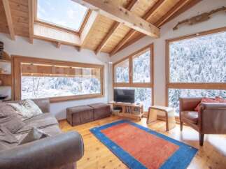 Experience the ultimate mountain retreat in this cozy living room, featuring a stunning panoramic view of snow-covered trees through expansive windows.