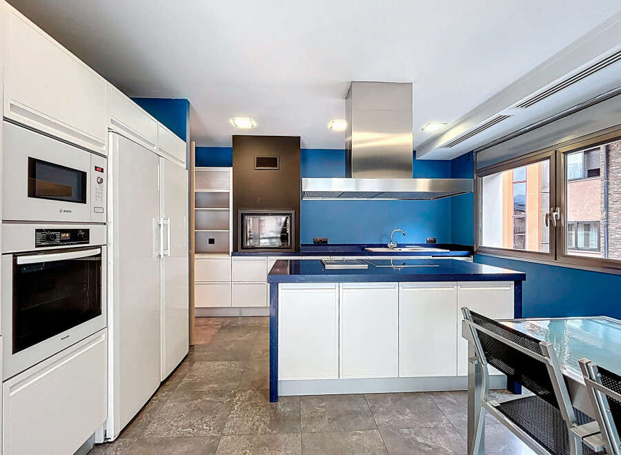 This modern kitchen boasts sleek white cabinetry and a striking blue accent wall, creating a stylish and inviting space.