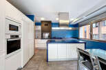 This modern kitchen boasts sleek white cabinetry and a striking blue accent wall, creating a stylish and inviting space.