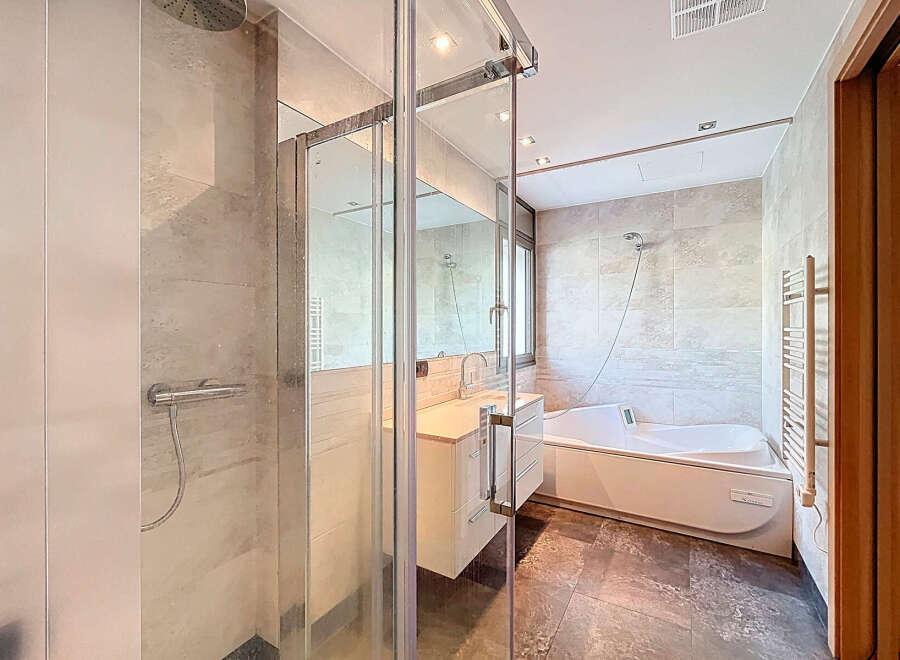 Step into luxury with this modern bathroom featuring a sleek glass shower enclosure and a relaxing bathtub.