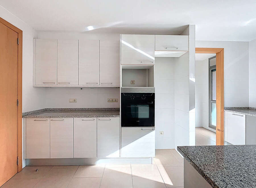 This modern kitchen boasts sleek white cabinetry and a granite countertop, offering a stylish and functional space for cooking and entertaining.
