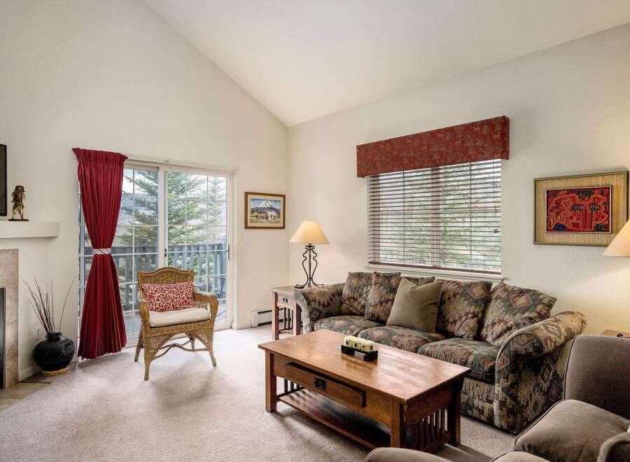 This cozy living room features a comfortable sofa, a charming wicker chair, and a beautiful view through the sliding glass door.