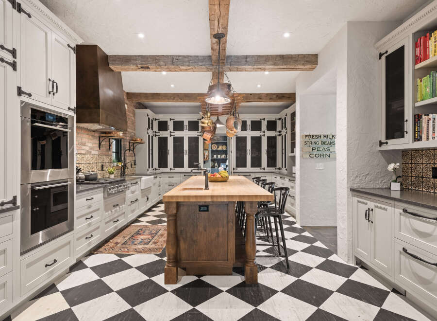 This stunning kitchen boasts a classic black and white checkered floor, complemented by elegant white cabinetry and a rustic wooden island.