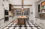 This stunning kitchen boasts a classic black and white checkered floor, complemented by elegant white cabinetry and a rustic wooden island.