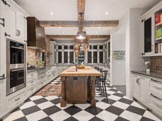 This stunning kitchen boasts a classic black and white checkered floor, complemented by elegant white cabinetry and a rustic wooden island.