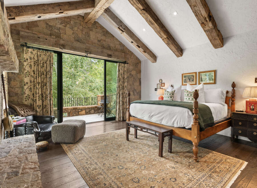 Experience luxury in this stunning bedroom featuring exposed wooden beams and a stone accent wall.