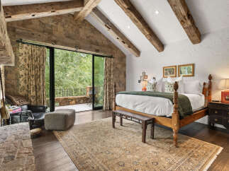 Experience luxury in this stunning bedroom featuring exposed wooden beams and a stone accent wall.