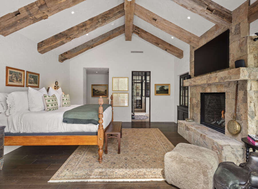 This stunning bedroom boasts a rustic charm with exposed wooden beams and a stone fireplace, creating a warm and inviting atmosphere.