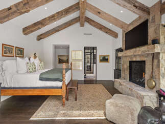 This stunning bedroom boasts a rustic charm with exposed wooden beams and a stone fireplace, creating a warm and inviting atmosphere.