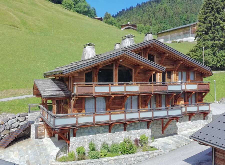 Experience luxury mountain living in this stunning wooden chalet, nestled against a vibrant green hillside.