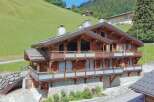 Experience luxury mountain living in this stunning wooden chalet, nestled against a vibrant green hillside.