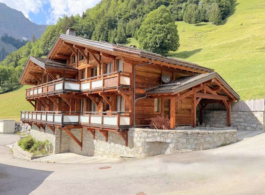 Experience luxury mountain living in this stunning wooden chalet, nestled against a lush green hillside.