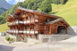 Experience luxury mountain living in this stunning wooden chalet, nestled against a lush green hillside.