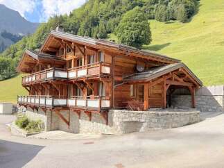 Experience luxury mountain living in this stunning wooden chalet, nestled against a lush green hillside.