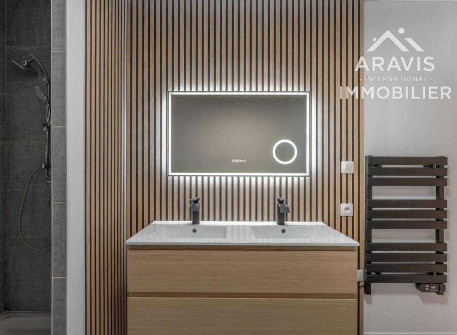 This modern bathroom features a sleek design with a wooden vanity and a stylish backlit mirror.