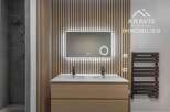 This modern bathroom features a sleek design with a wooden vanity and a stylish backlit mirror.